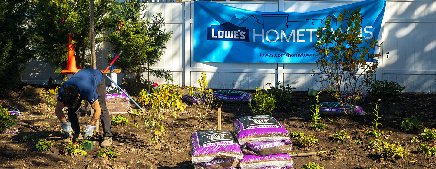 Lowe's associate gardening in front of Lowe's Hometowns sign