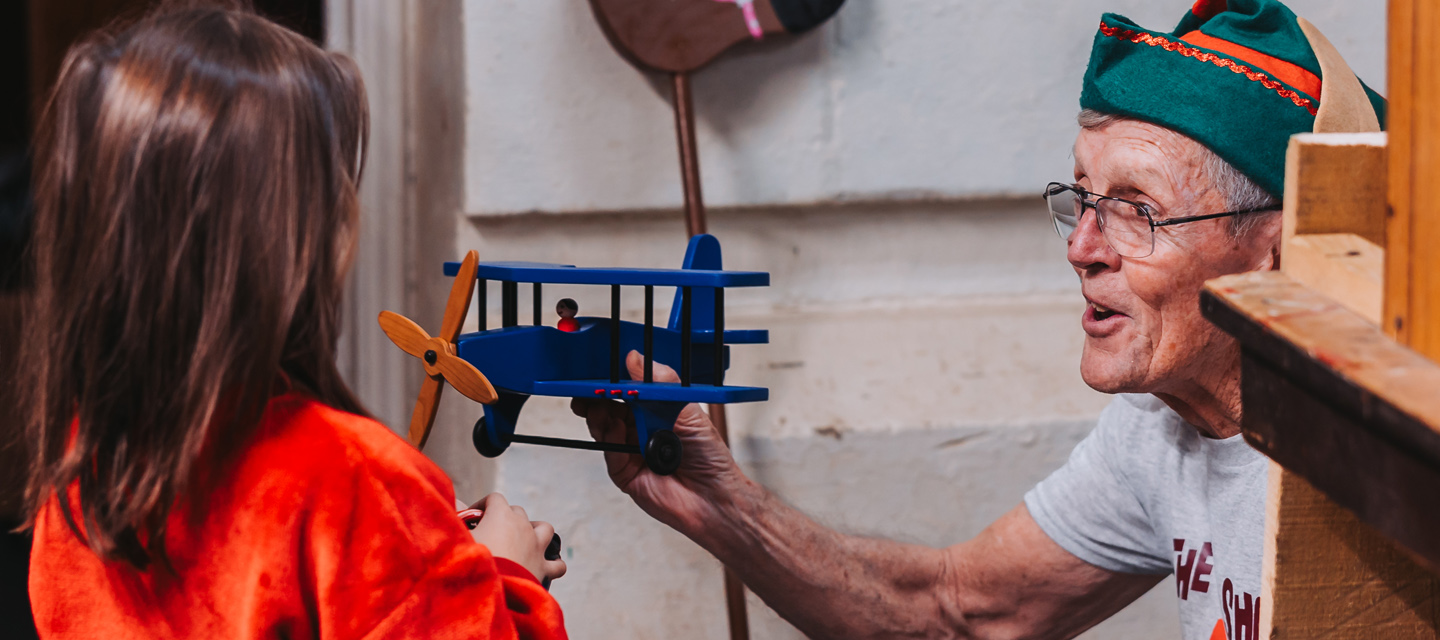 "Volunteer shows young girl a wooden toy airplane"